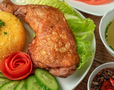 Cơm gà xối mỡ là một món ăn hấp dẫn, nổi bật bởi hương vị đậm đà và cách chế biến đặc trưng, mang đến trải nghiệm ẩm thực khó quên cho người thưởng thức. Ngay từ cái nhìn đầu tiên, đĩa cơm gà đã gây ấn tượng với phần cơm vàng óng, tơi xốp, được nấu từ nước luộc gà nên mang hương thơm béo nhẹ rất riêng. Bên trên là miếng gà chiên giòn rụm, lớp da vàng giòn bắt mắt, thịt bên trong vẫn giữ được độ mềm và mọng nước, tạo nên sự tương phản thú vị giữa giòn và mềm. Điểm đặc biệt của món ăn nằm ở kỹ thuật “xối mỡ” – khi gà sau khi được chiên sẽ được rưới thêm lớp dầu nóng để lớp da trở nên giòn hơn, đồng thời dậy mùi thơm hấp dẫn. Khi cắn một miếng gà, lớp da giòn tan trong miệng, kết hợp với phần thịt gà ngọt tự nhiên, tạo cảm giác vừa đậm đà vừa béo nhẹ nhưng không hề ngấy. Phần cơm ăn kèm được nêm nếm vừa phải, hạt cơm rời, thấm vị, giúp cân bằng lại độ béo của gà chiên. Ngoài ra, cơm gà xối mỡ thường được ăn kèm với dưa leo, cà chua và một ít rau sống để tăng độ tươi mát. Nước chấm cũng là yếu tố quan trọng, thường là nước mắm pha chua ngọt hoặc xì dầu, giúp tăng thêm hương vị cho món ăn. Khi chan nhẹ nước chấm lên cơm hoặc chấm từng miếng gà, vị giác được kích thích mạnh mẽ bởi sự hòa quyện của nhiều tầng hương vị khác nhau. Không chỉ ngon miệng, cơm gà xối mỡ còn cung cấp nhiều năng lượng. Thịt gà giàu protein, giúp cơ thể phát triển và duy trì sức khỏe, trong khi cơm cung cấp tinh bột cần thiết cho các hoạt động hàng ngày. Món ăn này vì thế rất phù hợp cho những bữa ăn chính, đặc biệt là khi cần một bữa ăn no lâu và đầy đủ dưỡng chất. Trong nhịp sống hiện đại, cơm gà xối mỡ ngày càng trở nên phổ biến và được nhiều người yêu thích. Từ các quán ăn bình dân đến nhà hàng, món ăn này luôn có mặt trong thực đơn như một lựa chọn quen thuộc. Không chỉ đơn giản là một món ăn ngon, cơm gà xối mỡ còn thể hiện sự tinh tế trong cách chế biến và sự sáng tạo trong ẩm thực, mang lại cảm giác hài lòng và thỏa mãn cho người thưởng thức mỗi khi nhắc đến.